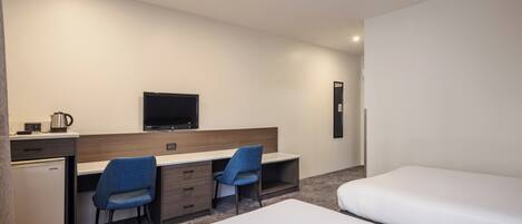 Habitación de hotel con cama, escritorio con dos sillas, televisor y un refrigerador pequeño.