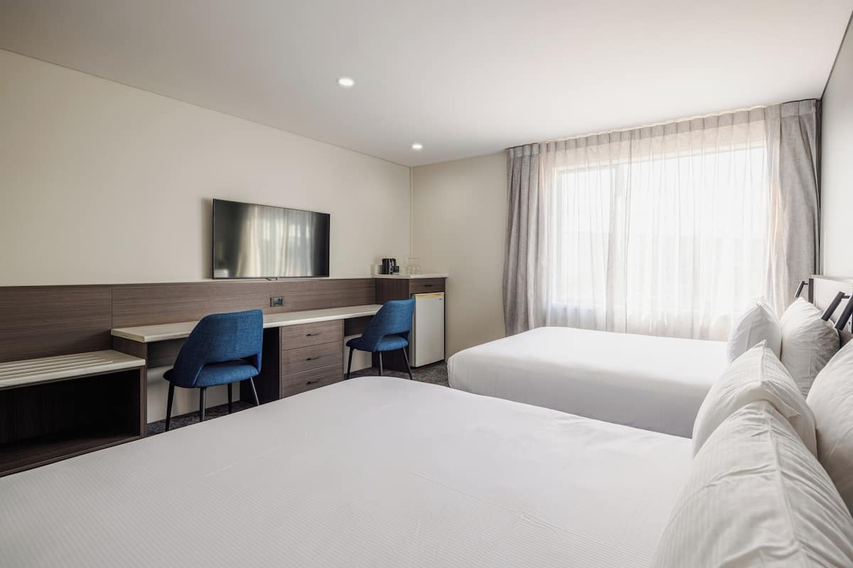 Hotelkamer met twee bedden, een bureau, een stoel, een televisie en een raam met gordijnen.