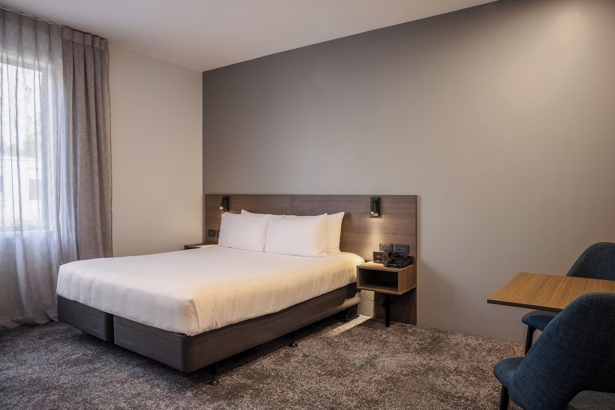 Een moderne hotelkamer met een groot bed, een nachtkastje met lamp, een klein bureau en een stoel.