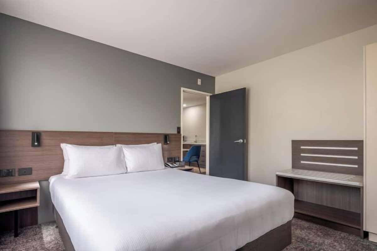Een hotelkamer met een groot bed, een nachtkastje, een bureau en een garderobe.