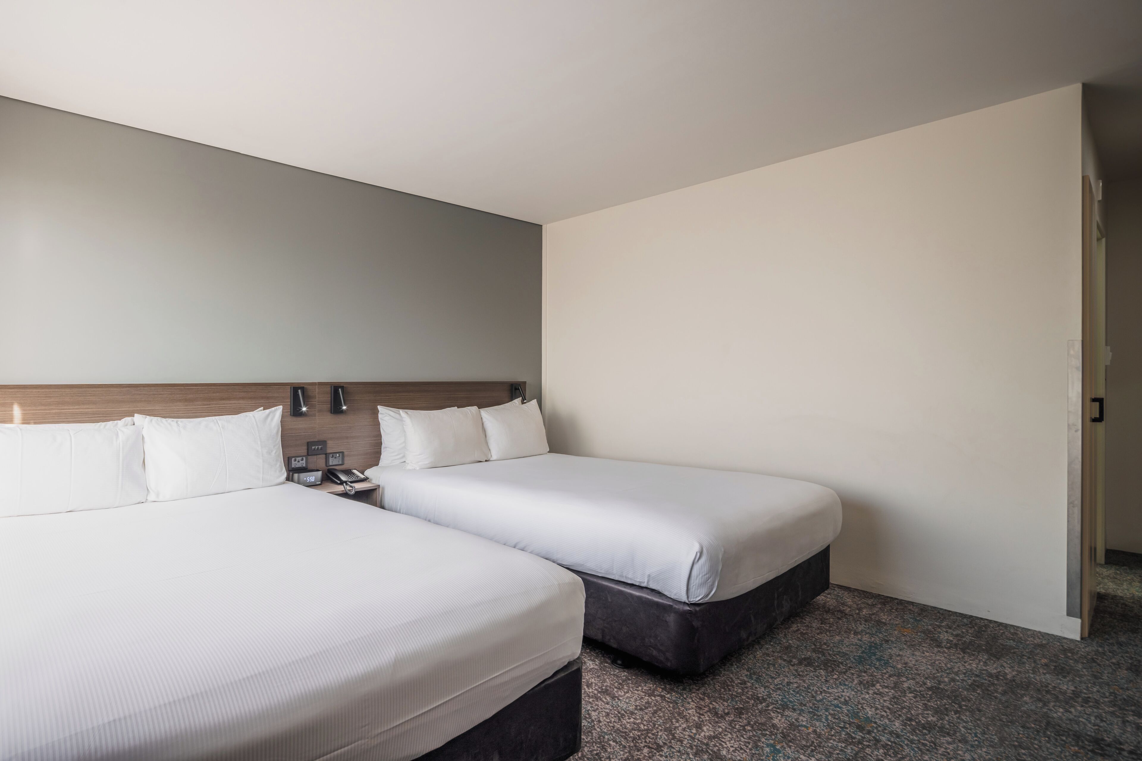 Habitación de hotel con dos camas, cabecera de madera, mesita de noche con teléfono y suelo alfombrado.