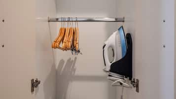 A wardrobe with a hanging rack, a shelf with an iron, and a storage bin.