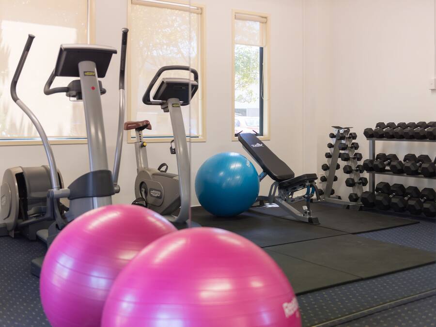 Ein Fitnessraum mit Trainingsgeräten, einem blauen Trainingsball, rosa Trainingsbällen und einem Hantelständer.
