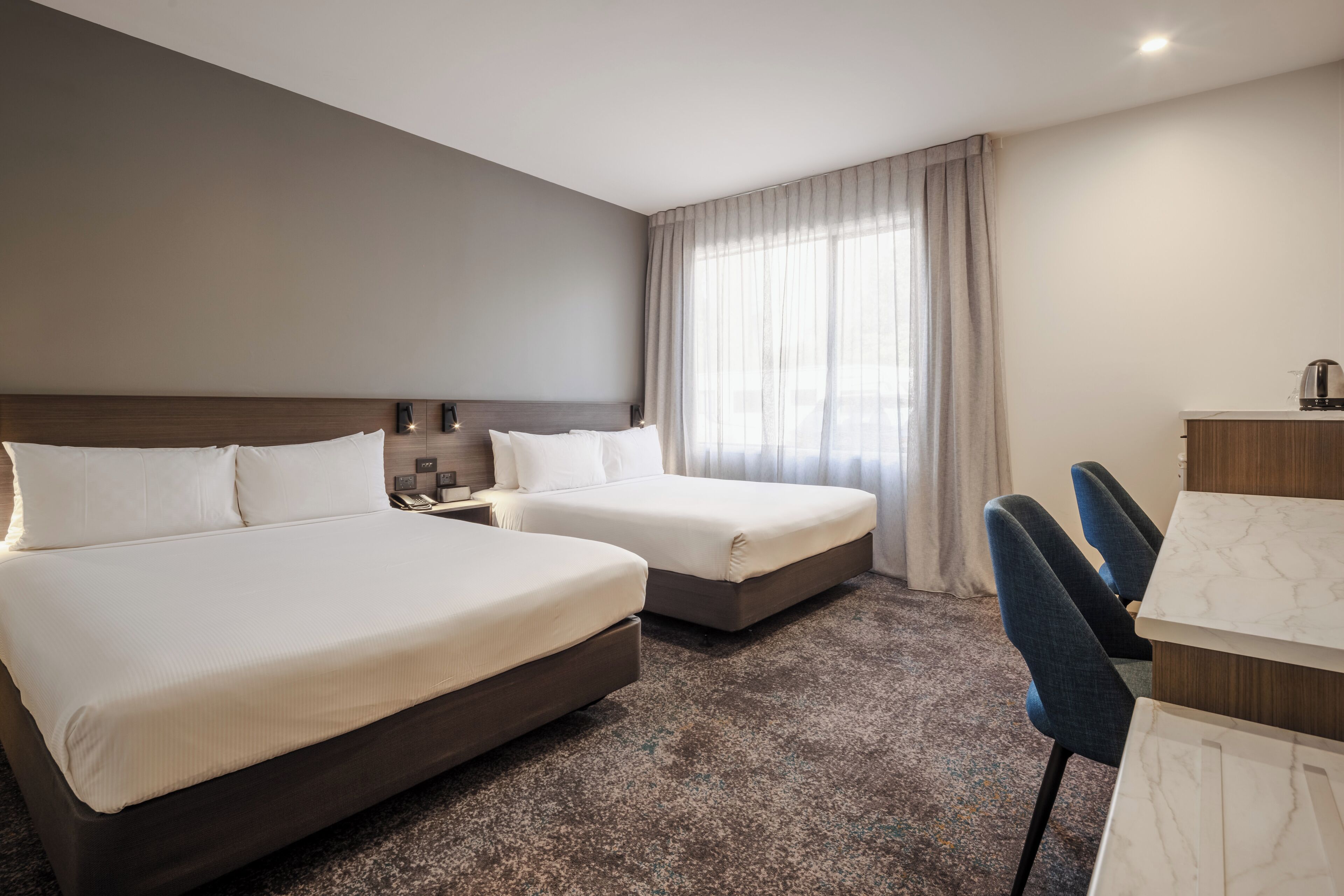 A hotel room with two beds, a desk, and a chair.