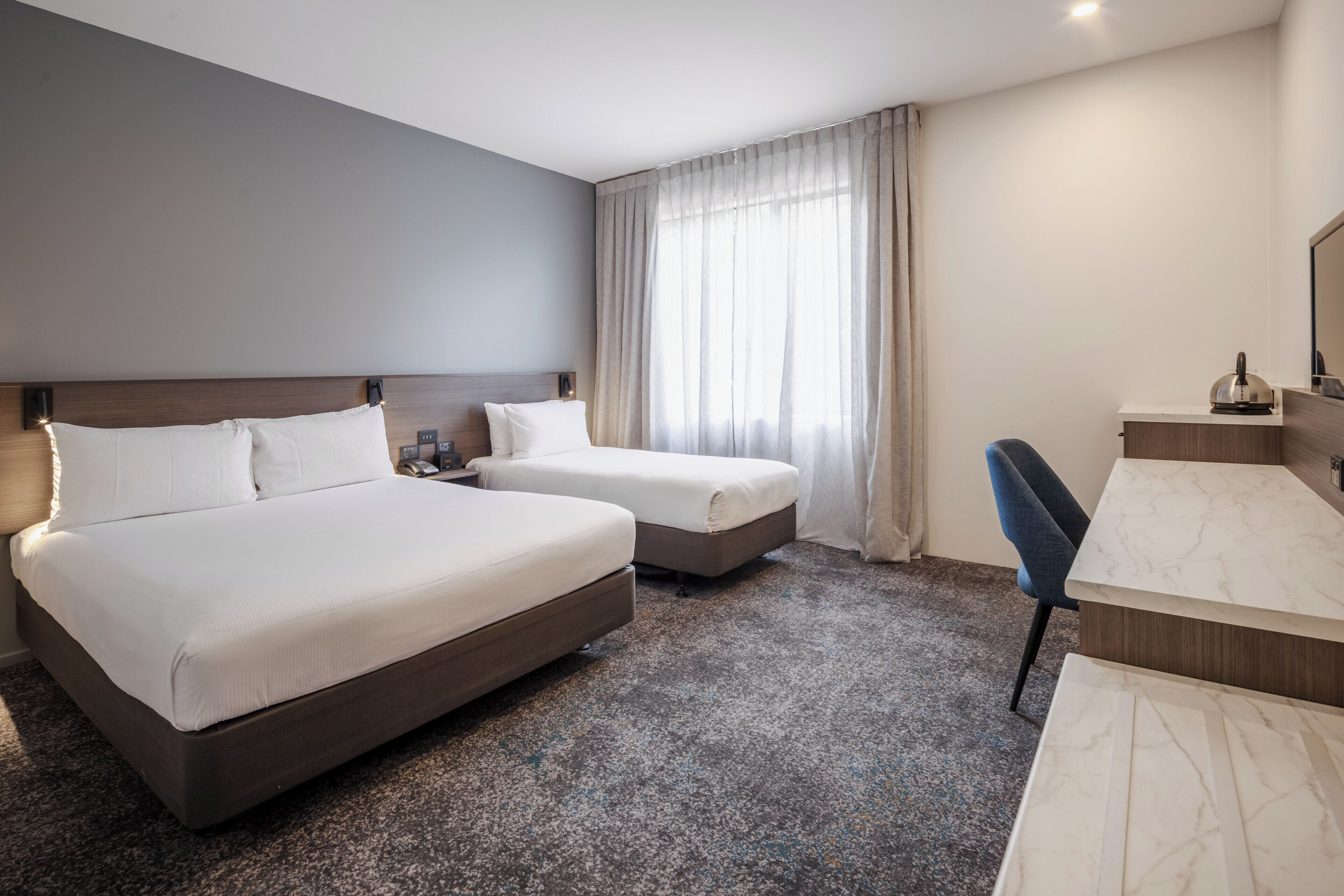 A hotel room with two beds, a desk, and a chair.