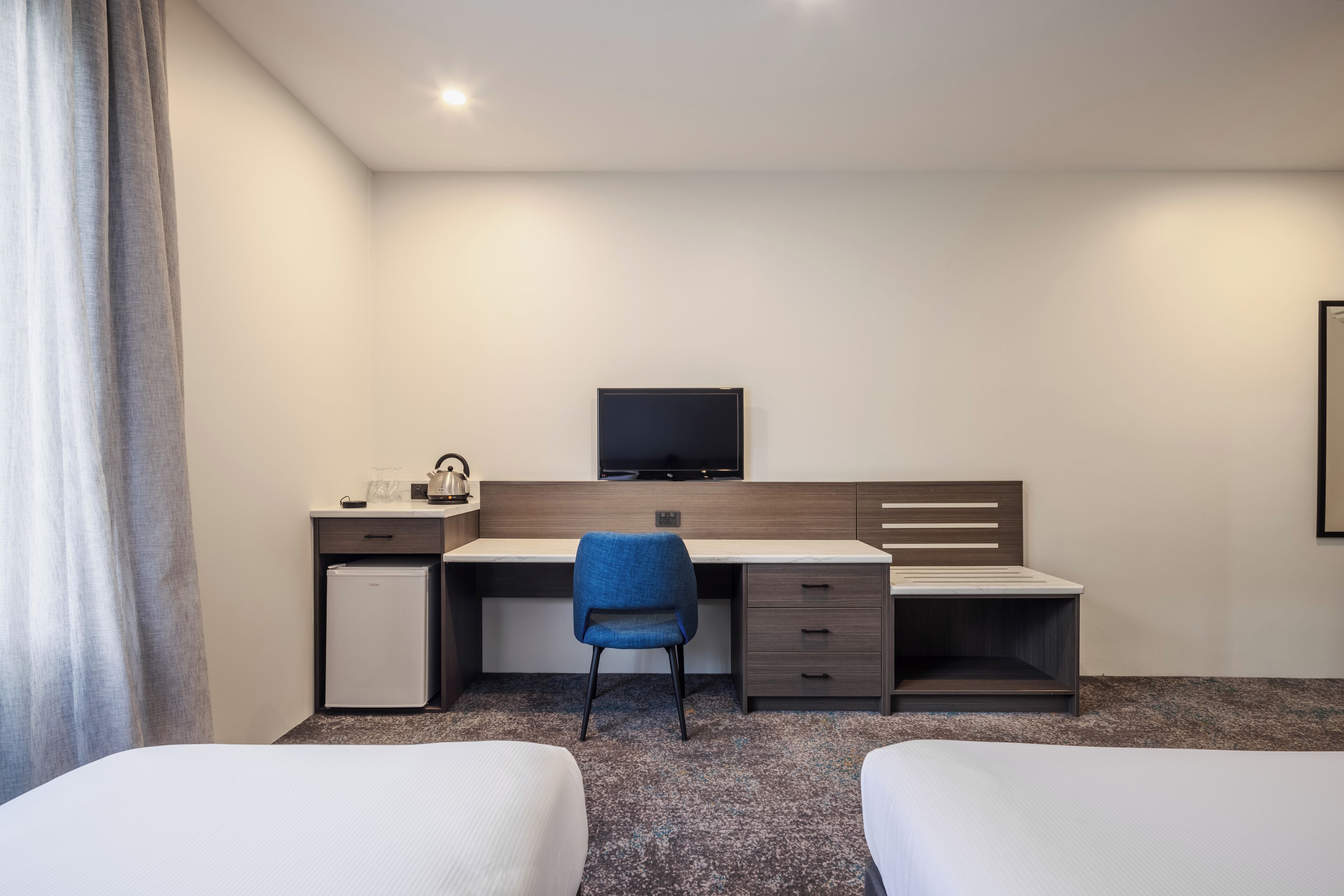 A hotel room with a bed, a desk with a chair, a television, and a small refrigerator.
