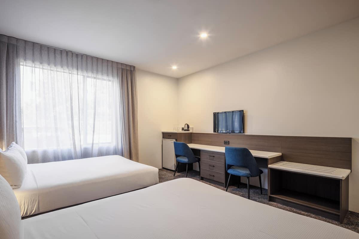 Een hotelkamer met twee bedden, een bureau, twee stoelen, een kleine koelkast en een televisie.
