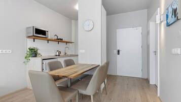 Una cocina moderna con microondas, lavaplatos y encimera de madera. Se aprecia una mesa de comedor con sillas y un reloj en la pared.