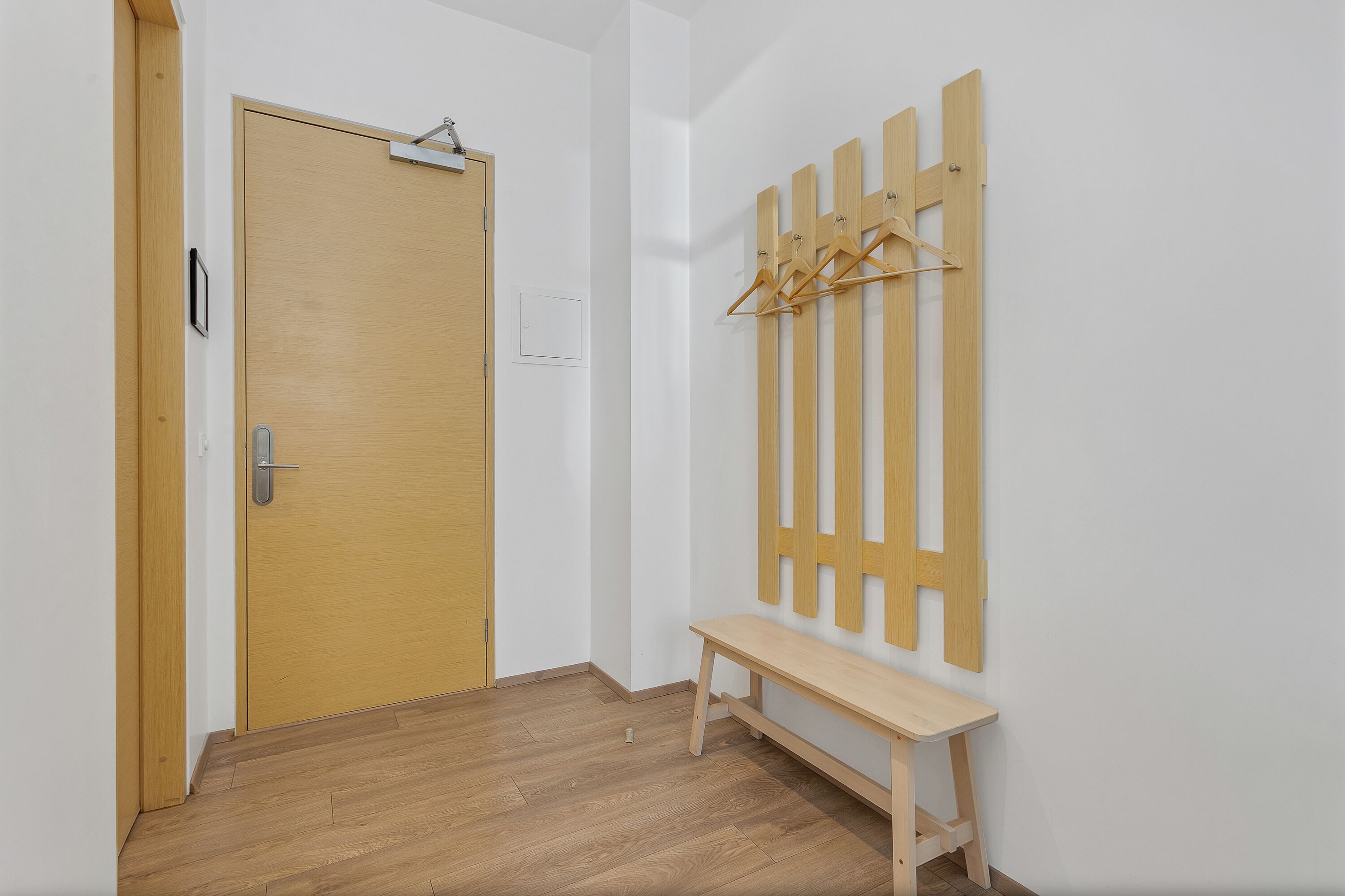 A hallway with a wooden door, a bench, and a wooden coat rack with hangers.