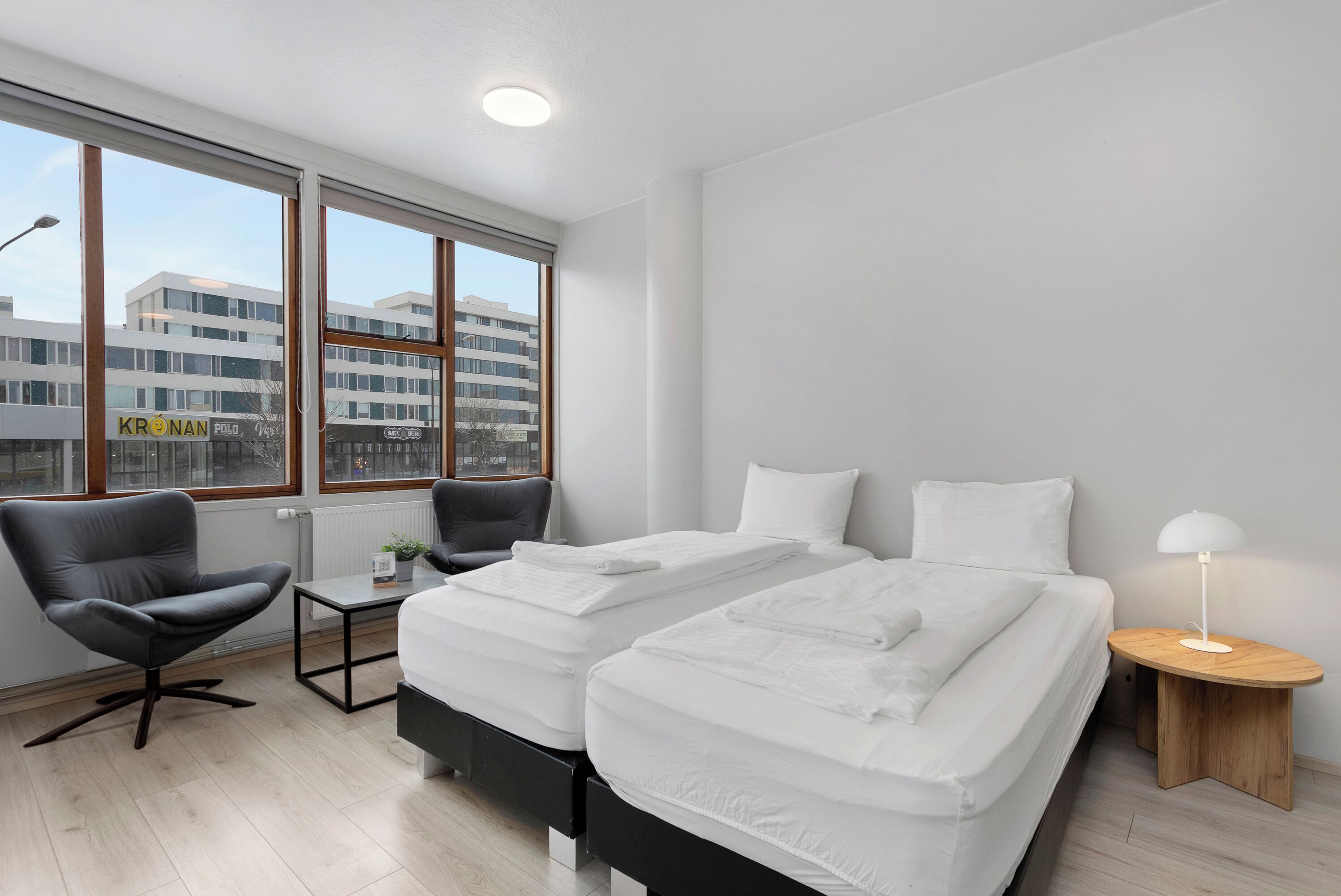 Una habitación de hotel moderna con dos camas, una silla, una mesita y una mesita de noche.