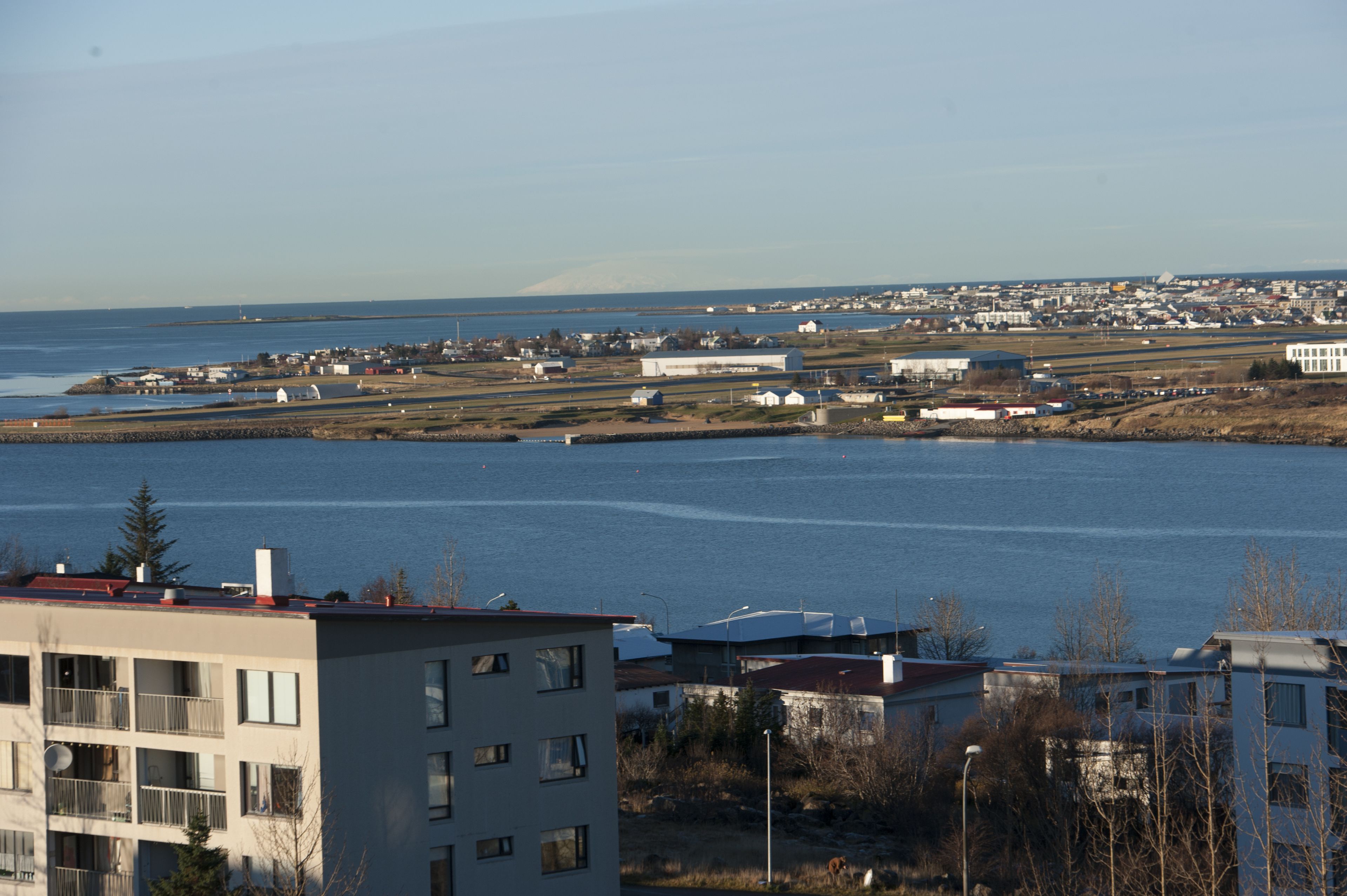 A coastal town with buildings near the water, including a multi-story building with balconies.