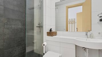 Un baño moderno con cabina de ducha de vidrio, un lavamanos blanco y un inodoro.