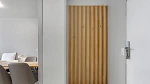 A modern room with a wooden slat partition, a dining area with chairs and a table, and a light fixture. - Iceland Comfort Apartments by Heimaleiga (Kópavogur)