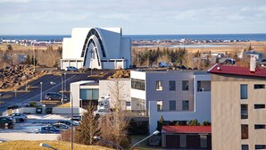A modern building with a unique arched design, surrounded by parking and other buildings, with a view of the sea in the background. - Iceland Comfort Apartments by Heimaleiga (Kópavogur)