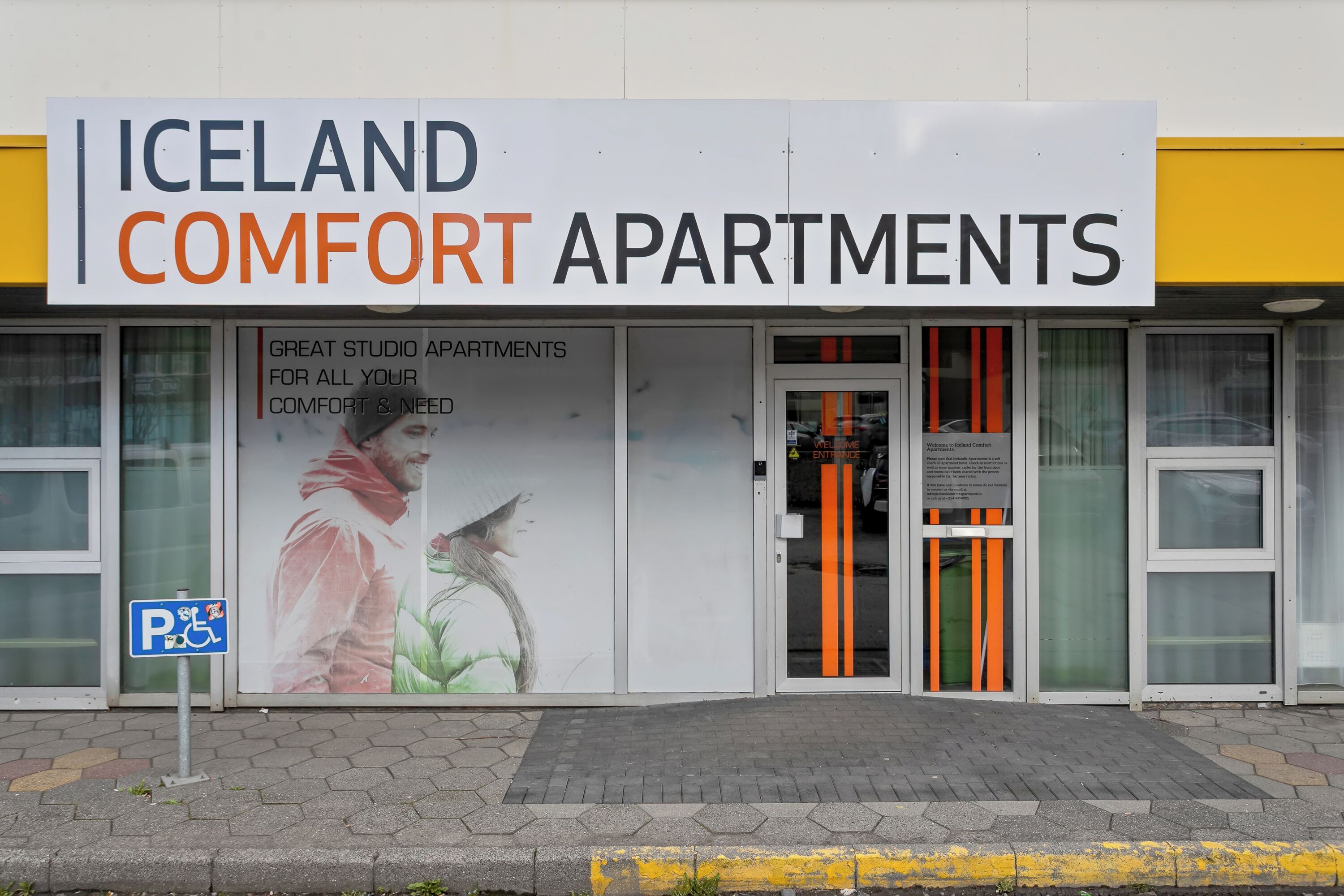Un immeuble avec une enseigne indiquant « Iceland Comfort Apartments » et un panneau signalant l’accessibilité aux personnes à mobilité réduite.