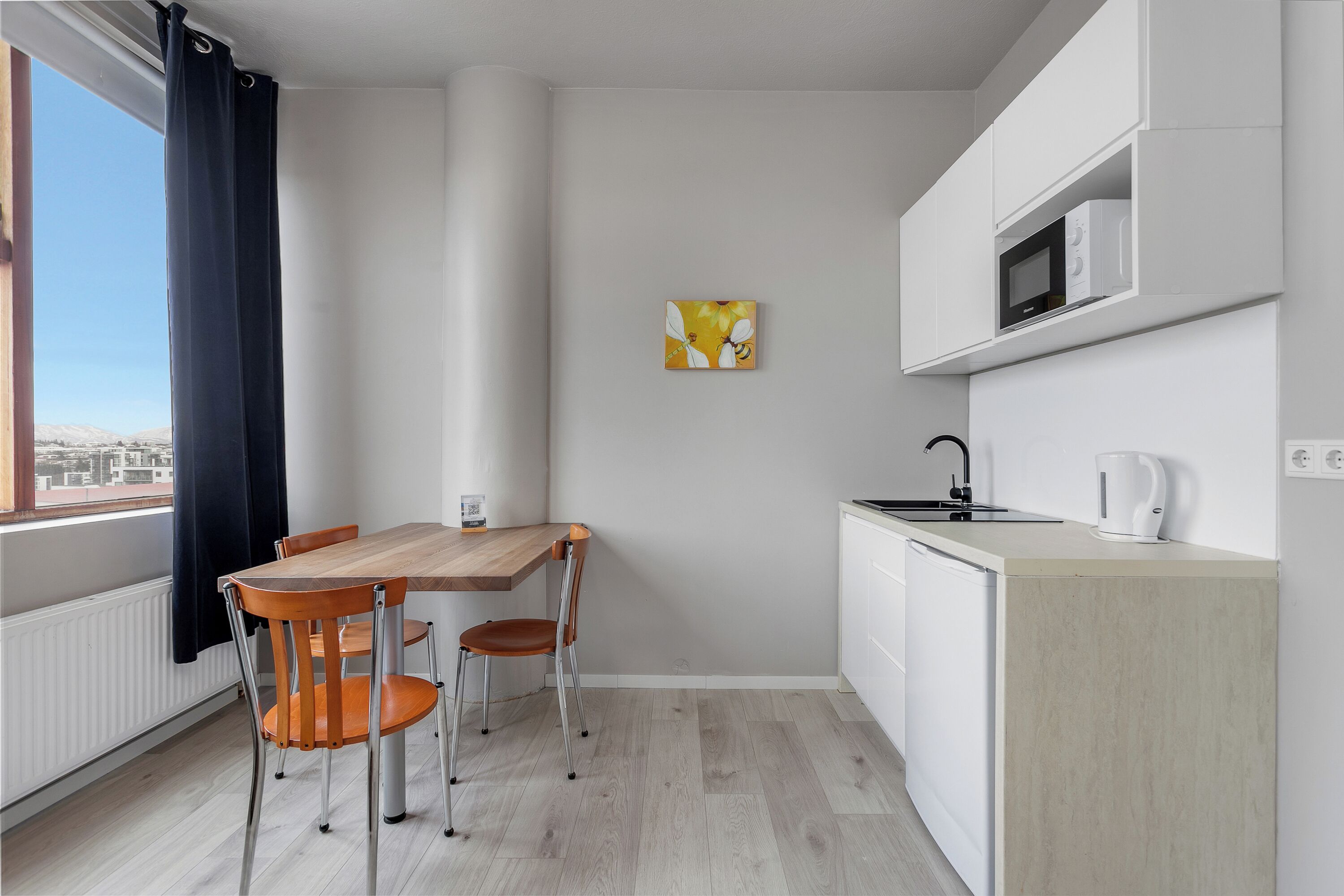 A compact kitchen with a wooden table and chairs, a microwave, and a kettle on the countertop.