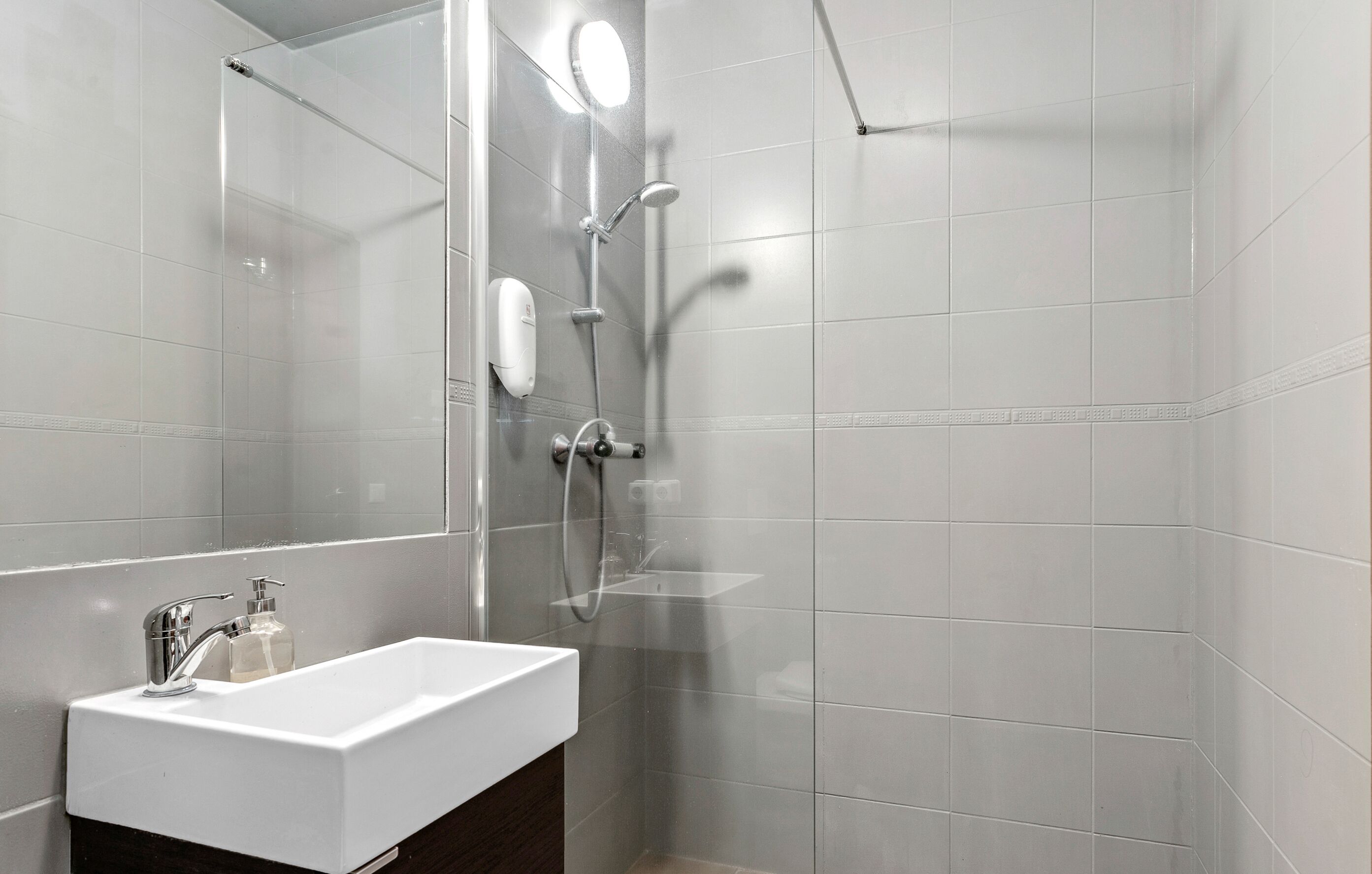 Un baño moderno con cabina de ducha de vidrio, un lavabo blanco y un espejo.