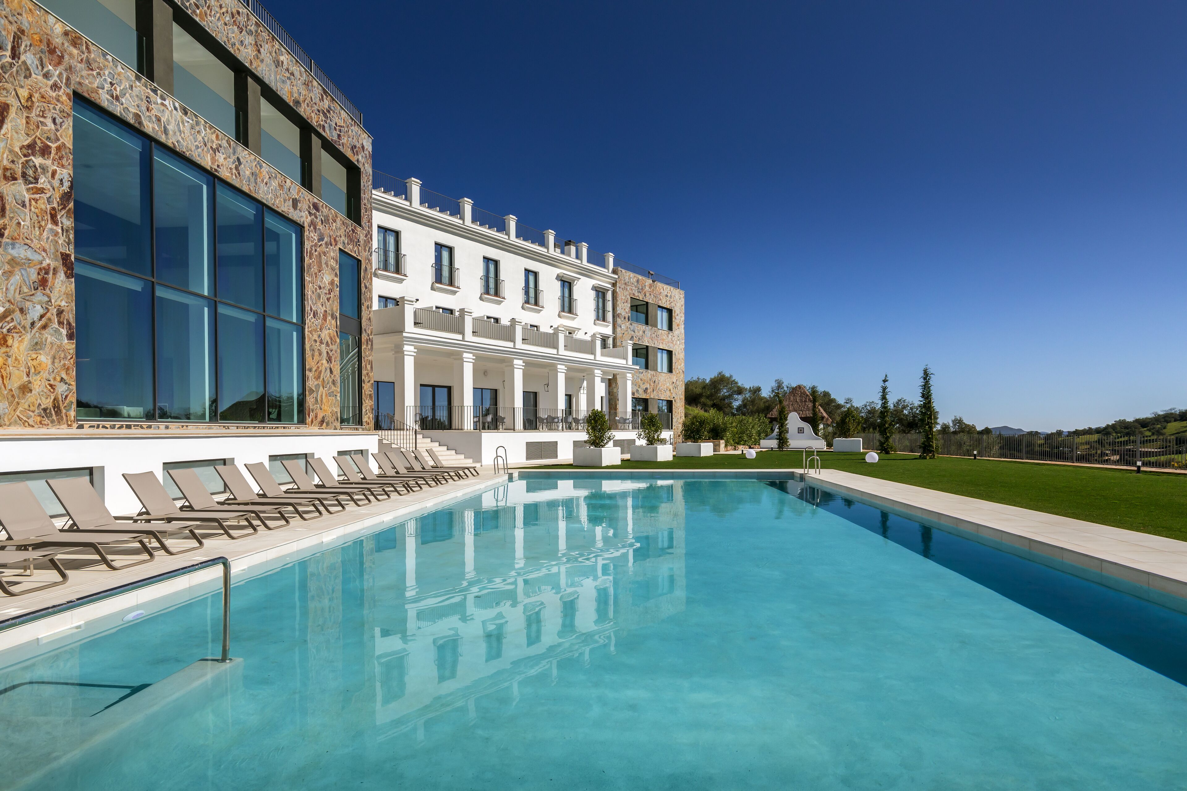 Un edificio moderno con piscina, ventanas amplias y un césped cuidado.