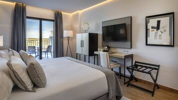 Een moderne hotelkamer met een groot bed, een bureau, een televisie en een balkon met zitplaatsen buiten.