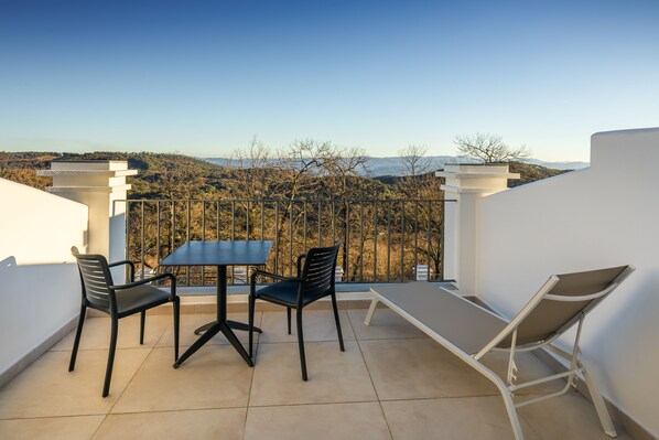 A balcony with a table and chairs, a lounge chair, and a view of a mountainous landscape.