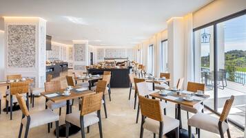 Un espace de restauration moderne avec des tables et des chaises, une cuisine en arrière-plan et de grandes fenêtres offrant une vue dégagée.