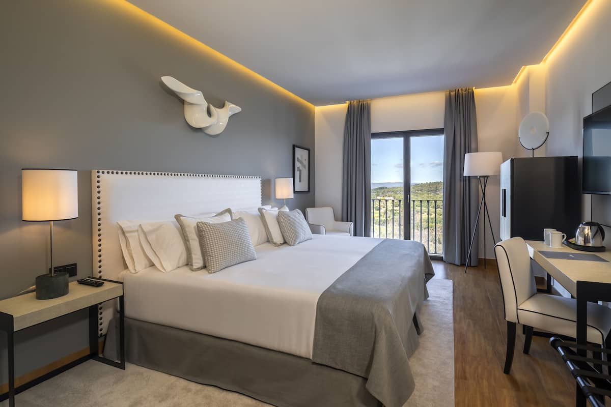 A modern hotel room with a large bed, bedside tables, a desk, and a chair.