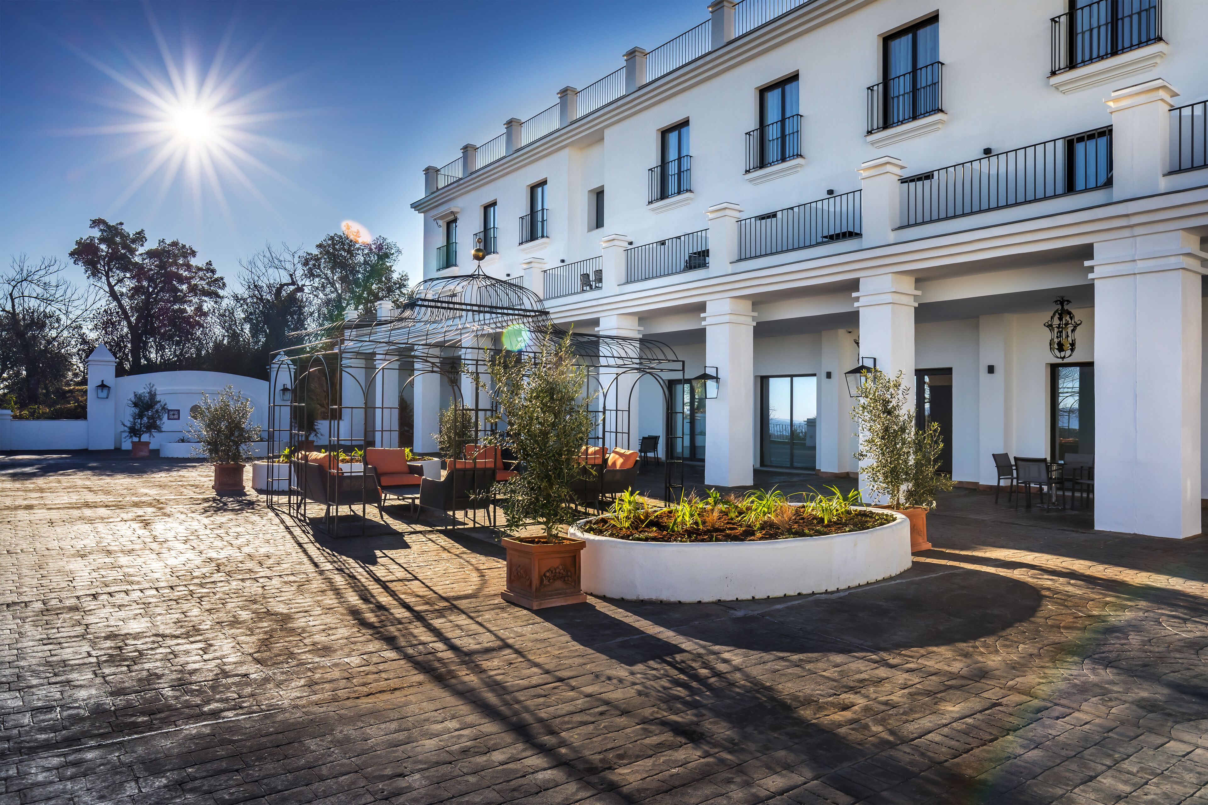 A hotel courtyard with a sunlit brick floor, a glass gazebo, and outdoor seating.