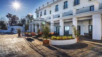 A hotel courtyard with a sunlit brick floor, a glass gazebo, and outdoor seating.