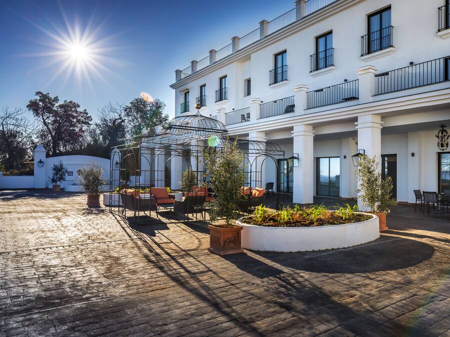 A hotel courtyard with a sunlit brick floor, a glass gazebo, and outdoor seating.