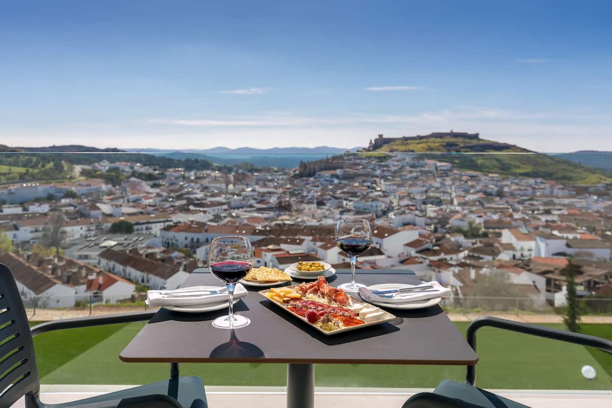 A table with a meal and wine glasses, overlooking a town with a hill and castle in the distance.