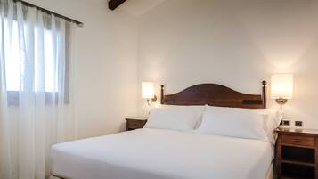 A neatly made bed with white linens, two bedside tables with lamps, and sheer curtains on a window.