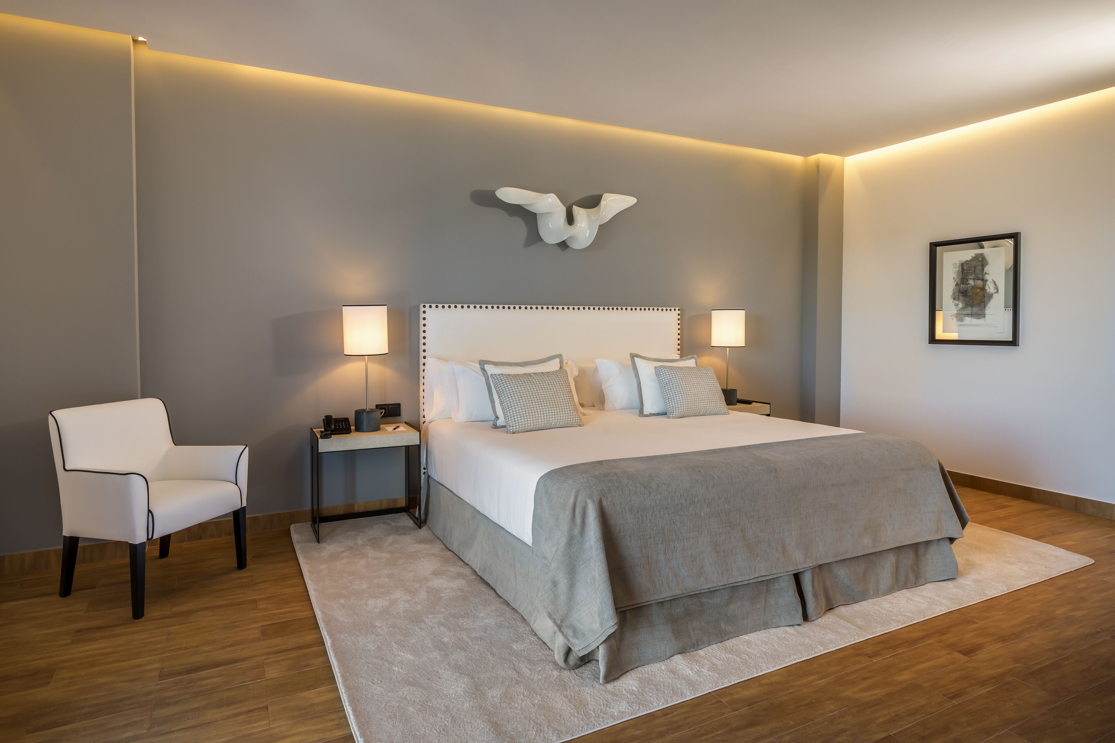 Quarto moderno com cama grande, luminárias de cabeceira, uma cadeira e um aplique.