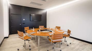 Un salón de conferencias con una mesa redonda, seis sillas y una televisión de pantalla plana en la pared.