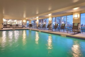 Una piscina interior con agua cristalina, rodeada de sillones de descanso y grandes ventanales que ofrecen vistas al exterior.