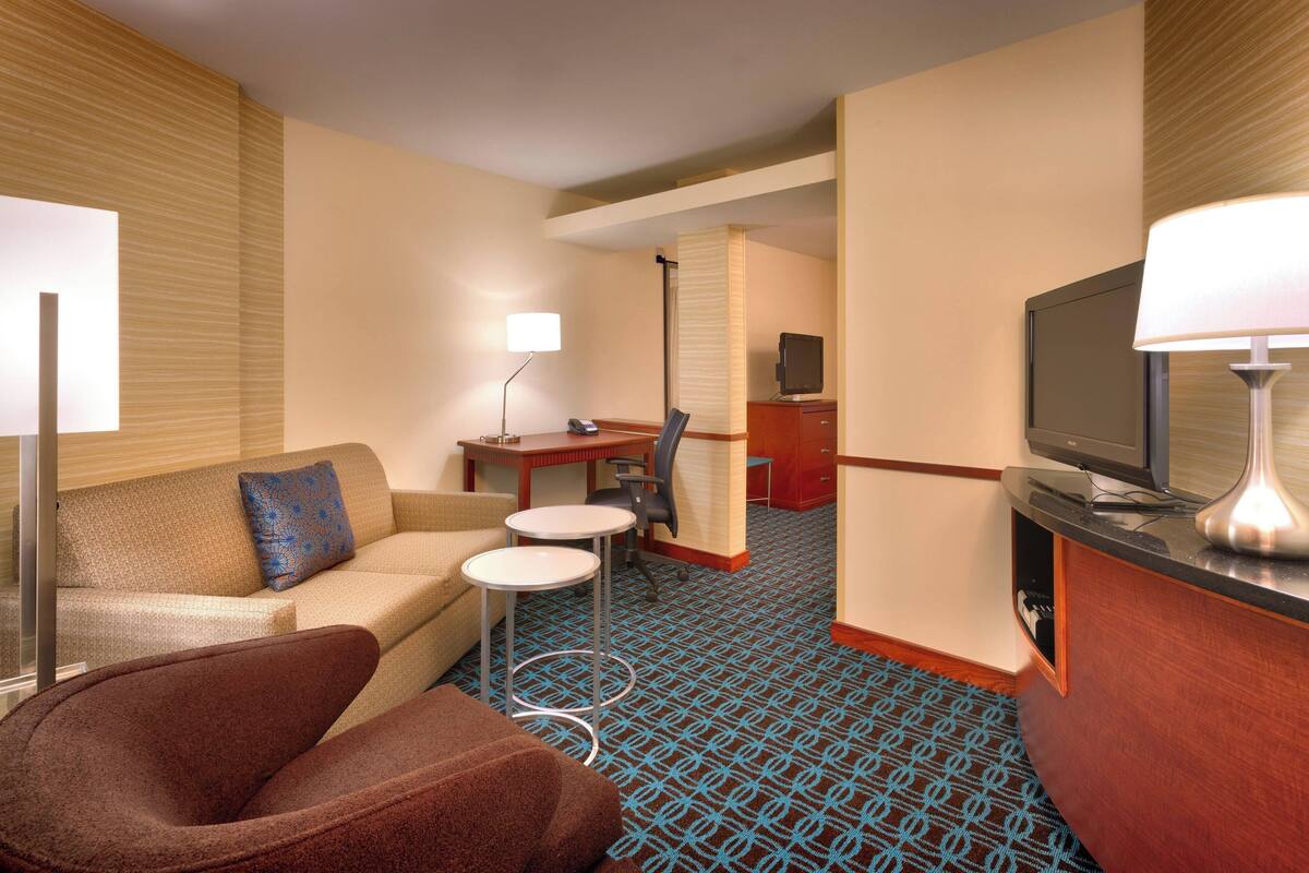 Habitación de hotel con sofá, una mesita, televisión y escritorio con silla.