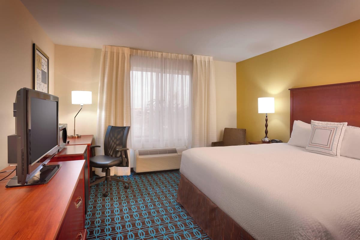 Habitación de hotel con cama, escritorio con computadora, silla, televisor y ventana con cortinas.