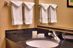 Ein Badezimmer mit Waschbecken, Spiegel, Handtüchern und Pflegeprodukten.