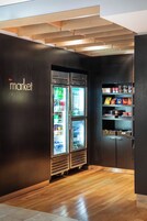 Un interior moderno con suelo de madera, una vitrina refrigerada y una estantería llena de aperitivos.