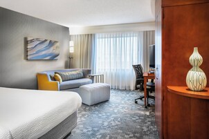 Habitación de hotel con una cama grande, un sofá, un reposapiés, un escritorio y una lámpara.