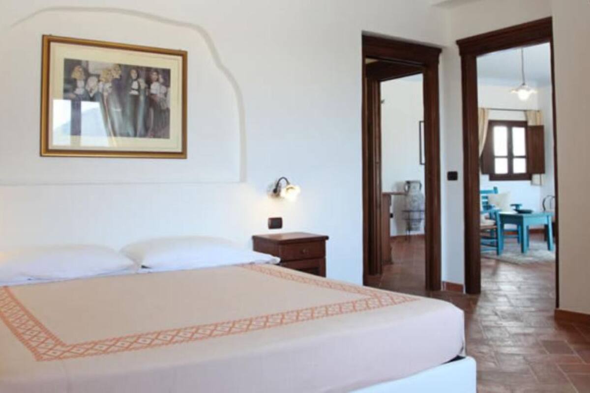 Una habitación de hotel con una cama, una mesita de noche, una lámpara de pared y un cuadro enmarcado.