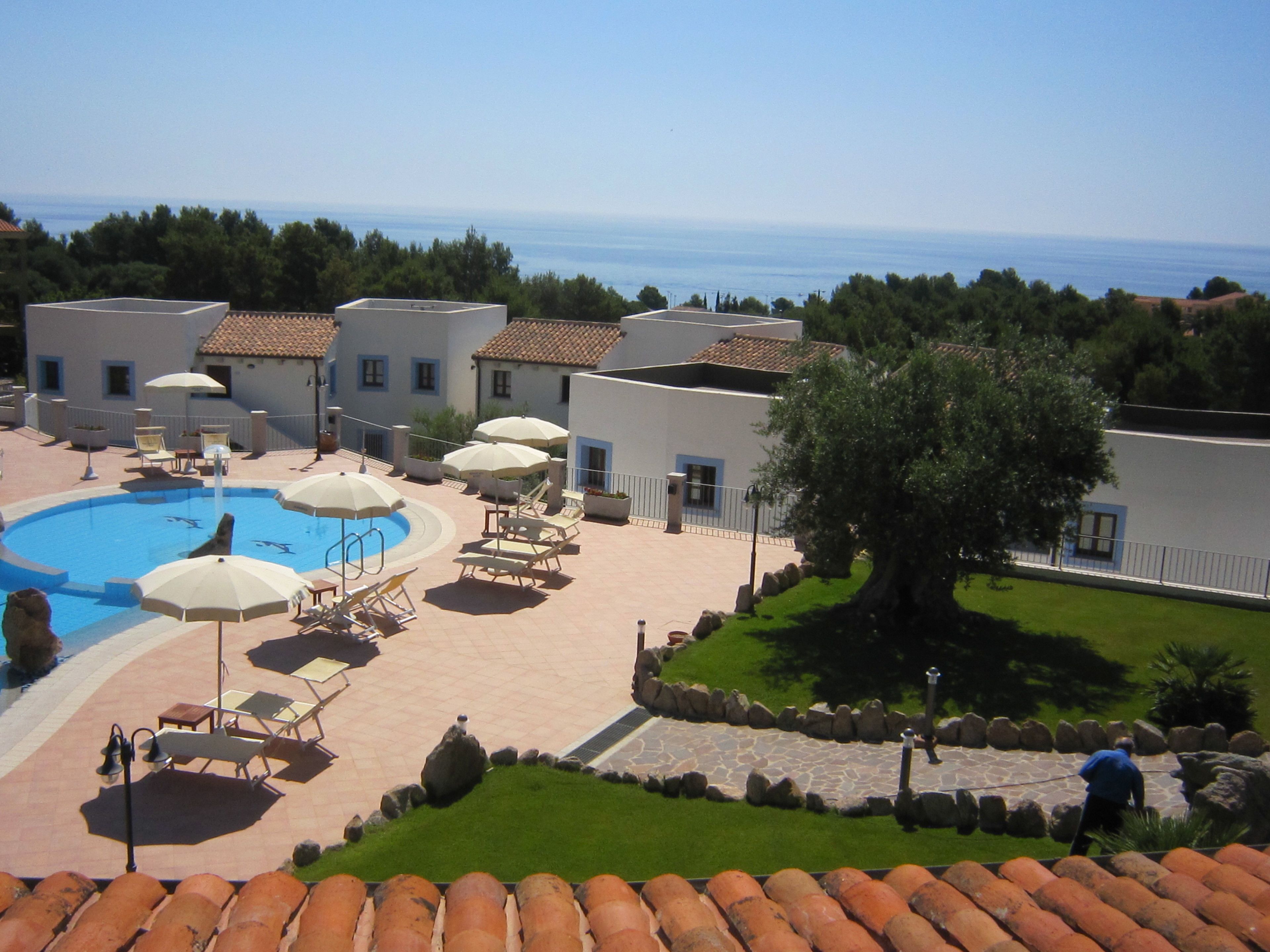 A pool area with lounge chairs and umbrellas, a stone pathway, and a view of the sea.
