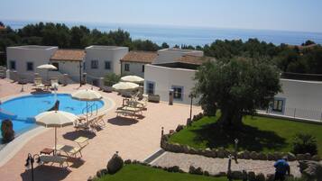 A pool area with lounge chairs and umbrellas, a stone pathway, and a view of the sea.
