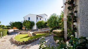 A white building with a stone pathway leading to a well-maintained garden. - Hotel Nuraghe Arvu (Dorgali)