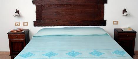 A bedroom with a large wooden headboard, a light blue bedspread with floral patterns, two bedside tables with books, and wall-mounted lamps.