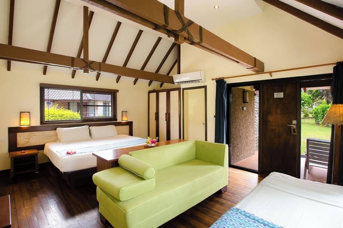 A bedroom with a bed, a green sofa, a window with a view, and a door leading to an outdoor area.