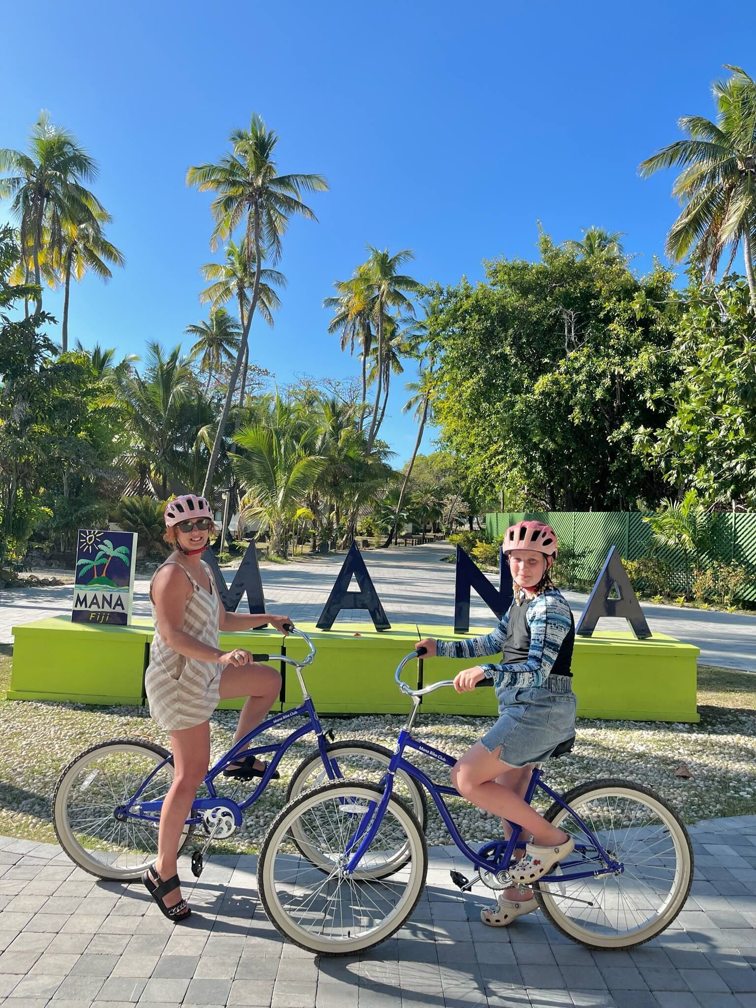Two people on bicycles in front of a sign with the letters "MANANA".
