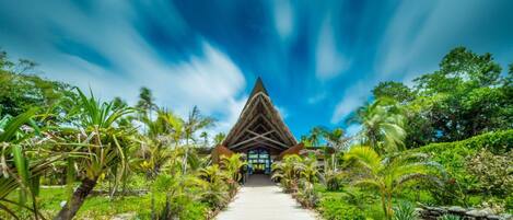 A pathway leading to a building with a triangular roof, surrounded by tropical vegetation.