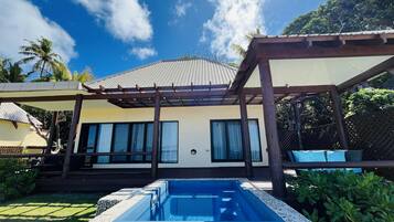 A pool with a pebble border, a covered patio area, and a building with large windows and a sloped roof.