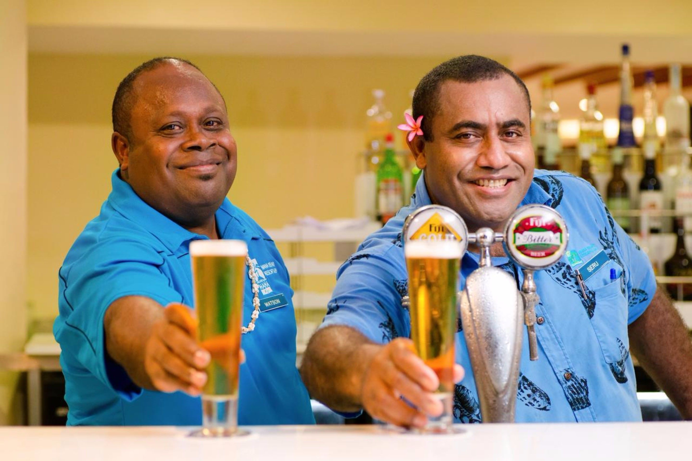 Two individuals in blue shirts at a bar, each holding a beer glass.