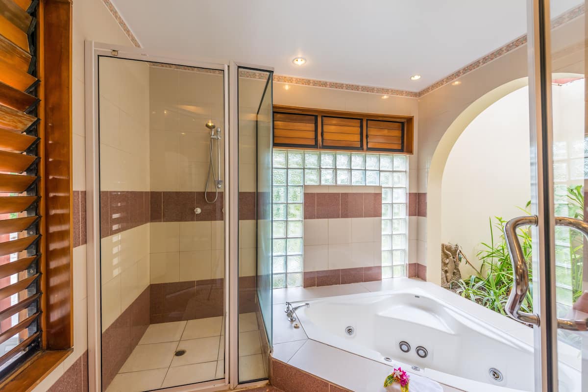 A bathroom with a glass-enclosed shower, a large bathtub, and a window with a view of greenery.